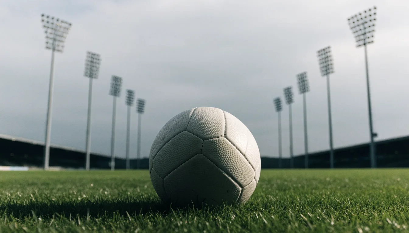 Ein Fußball auf einem Rasenplatz, im Hintergrund Flutlichtmasten und ein bewölkter Himmel.