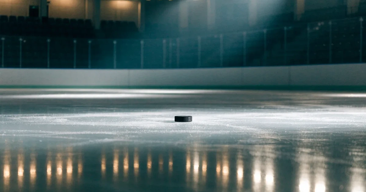 Eine leere Eisfläche in einer Halle mit Banden und Flutlicht, auf dem Eis liegt ein einzelner Puck.