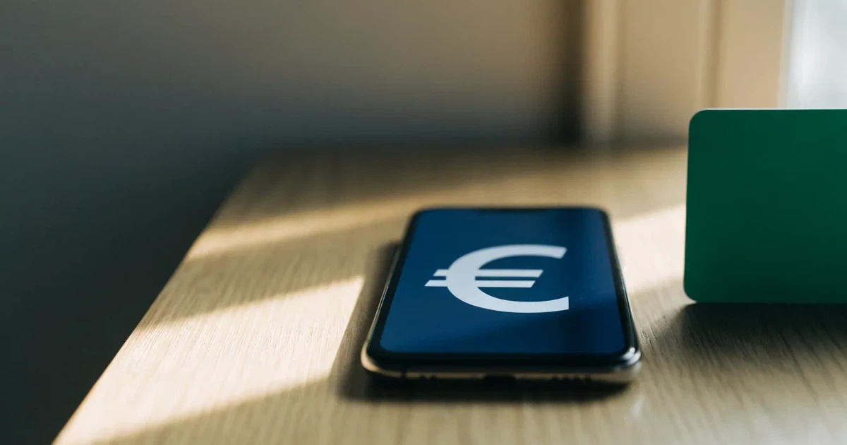 Eine Plastikkarte ohne Aufdruck liegt neben Münzen und einem Smartphone mit dunklem Display auf einem hellen Tisch.